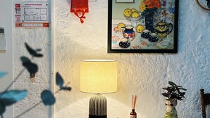 Een gezellige kamer met een witte muur, een lijst met een schilderij, een tafellamp en een kleine plant in een pot.