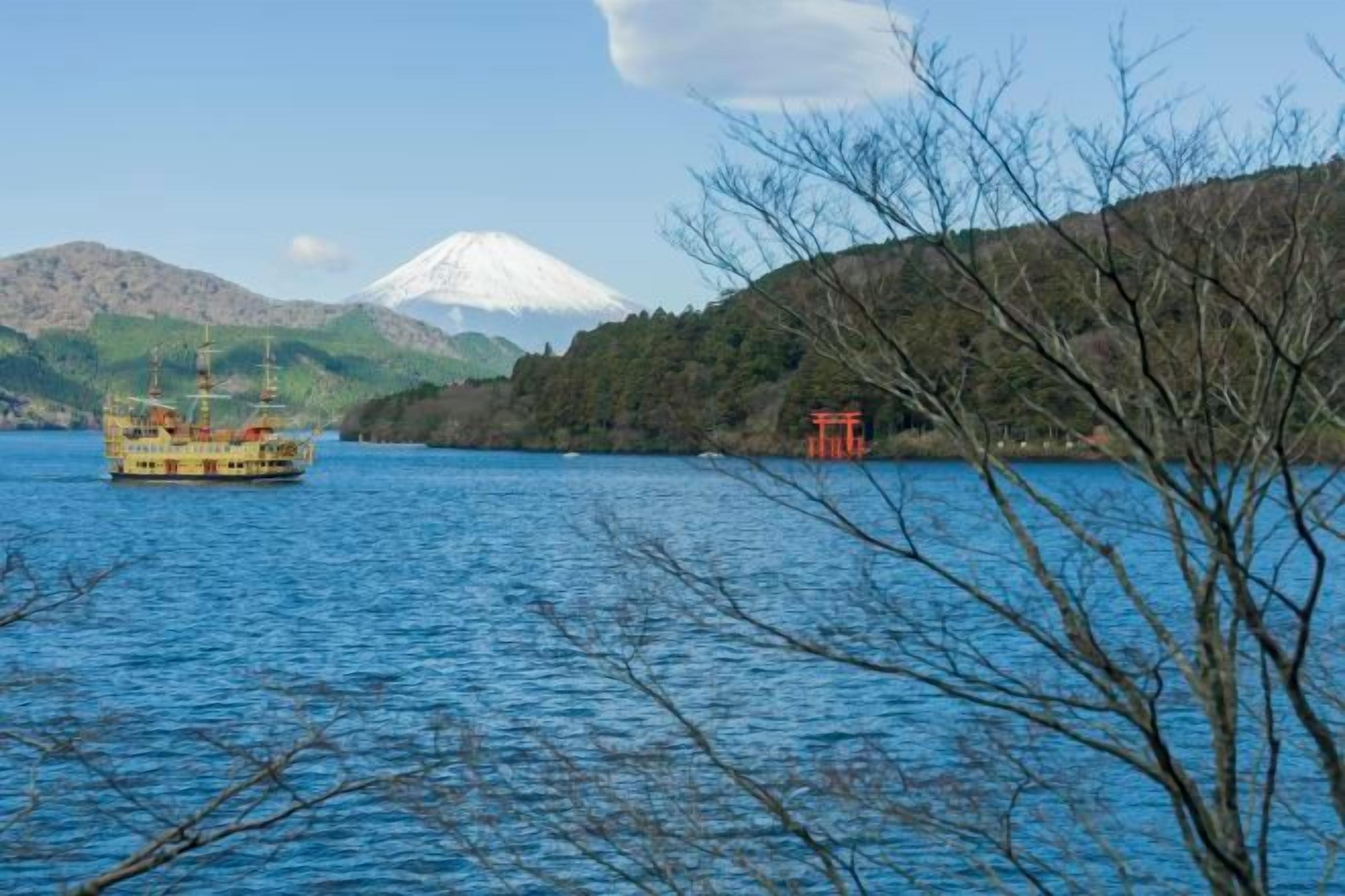 A boat on a lake with a mountain in the background and a red structure on the shore.