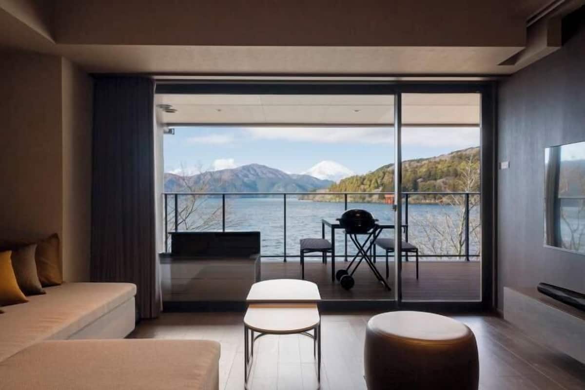 A modern room with a large sliding glass door leading to a balcony with a view of mountains and a lake.