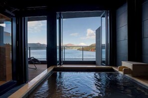 Ein Wellnessraum mit Whirlpool, großen Fenstern und Blick auf das Wasser.
