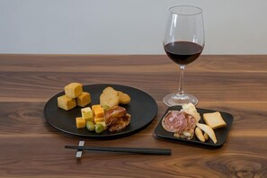 Une table en bois sur laquelle se trouvent une assiette noire de fromage et un verre de vin rouge.
