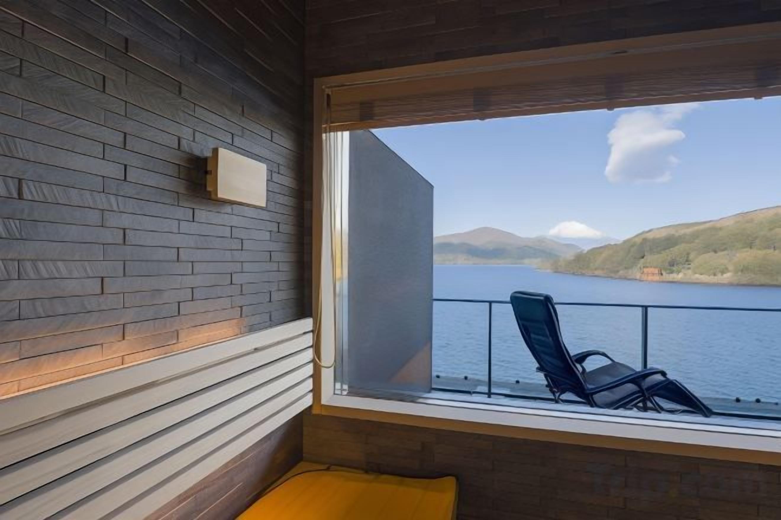 A room with a view of a lake, a chair, and a wooden wall.