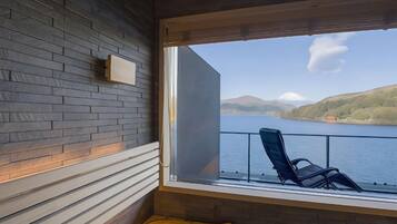 A room with a view of a lake, a chair, and a wooden wall.