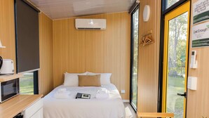 Een moderne hotelkamer met een bed, een klein bureau, een magnetron en een raam met uitzicht op groen.