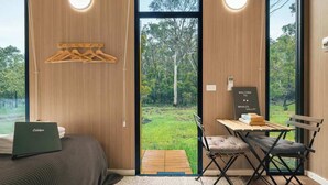 A modern room with a bed, a desk with a laptop, and a view of a forest through large windows. - Brisbane Ranges Hideaway by Tiny Away (Steiglitz)