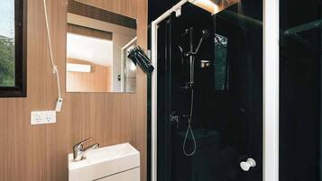 A modern bathroom with a wooden vanity, a glass shower enclosure, and a visible outdoor view.