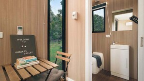 A modern bathroom with a sink, mirror, and toilet. There's a wooden bench with a welcome sign and books. - Brisbane Ranges Hideaway by Tiny Away (Steiglitz)