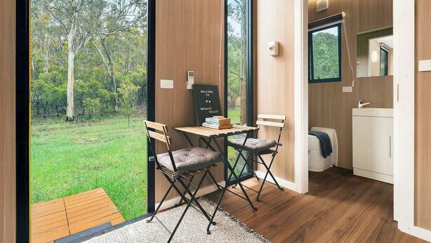 A modern room with a large window, a small table with chairs, and a view of a forest. - Brisbane Ranges Hideaway by Tiny Away (Steiglitz)