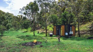 A small cabin with a yellow door, surrounded by trees and grass, with a fire pit and outdoor furniture. - Brisbane Ranges Hideaway by Tiny Away (Steiglitz)