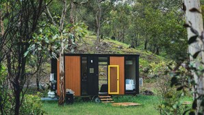 A small, modern cabin with a wooden exterior, large windows, and a yellow door, situated in a forested area. - Brisbane Ranges Hideaway by Tiny Away (Steiglitz)