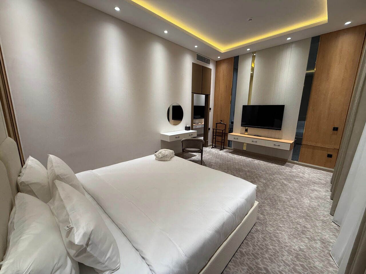 A modern hotel room with a large bed, a desk, a TV, and a mirror.
