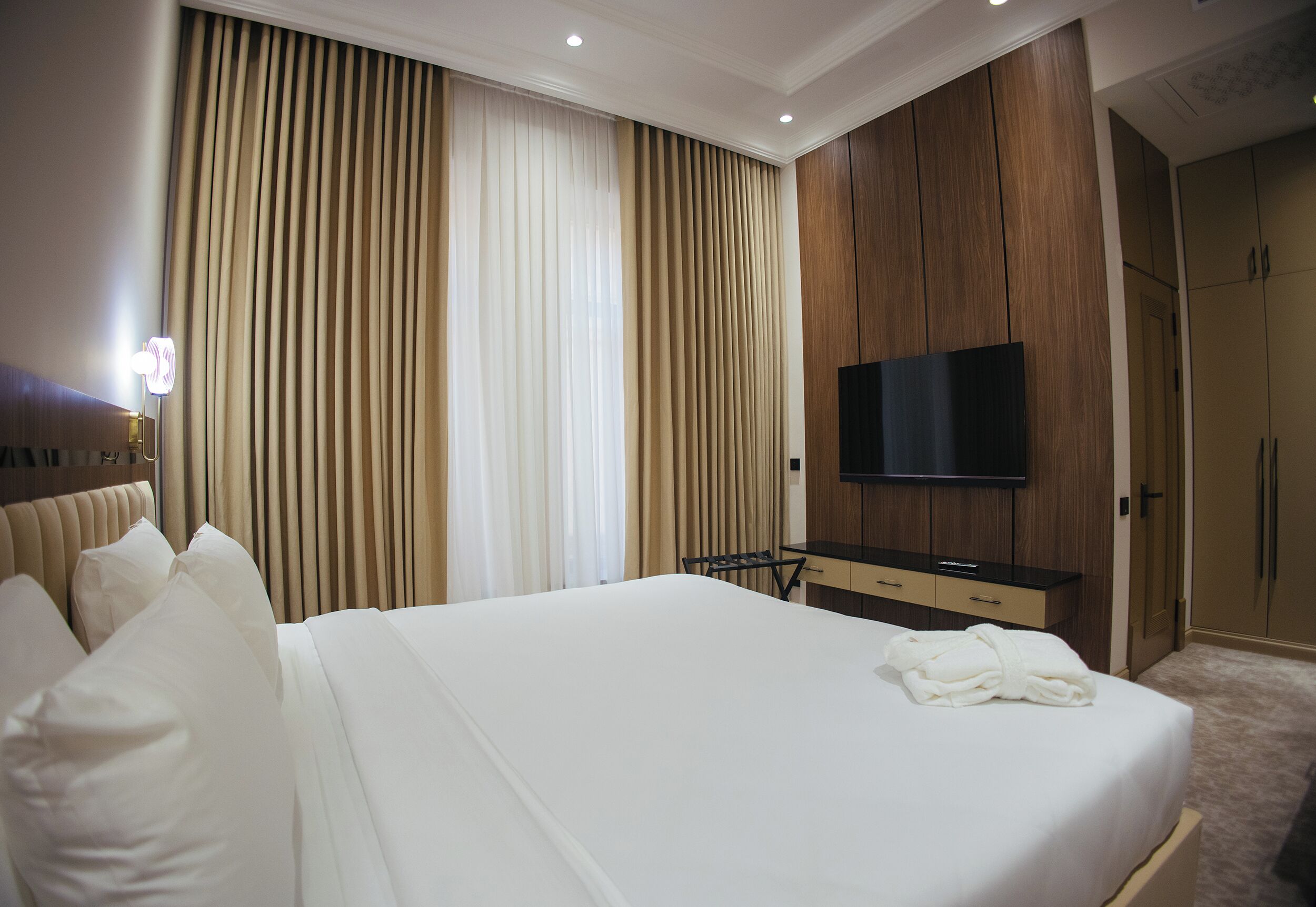 Une chambre d’hôtel avec un grand lit, un téléviseur fixé au mur, un bureau avec une chaise et une armoire.