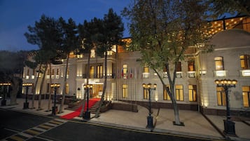 A grand hotel with a red carpet entrance, multiple flags, and classic architecture.