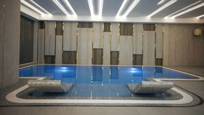 A modern indoor swimming pool with a clear blue water surface, surrounded by a tiled floor and a series of recessed lights on the ceiling. - AD Bellagio Hotel (Samarkand)