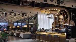A modern bar area with a curved counter, bar stools, and a large television screen displaying a cityscape. - AD Bellagio Hotel (Samarkand)