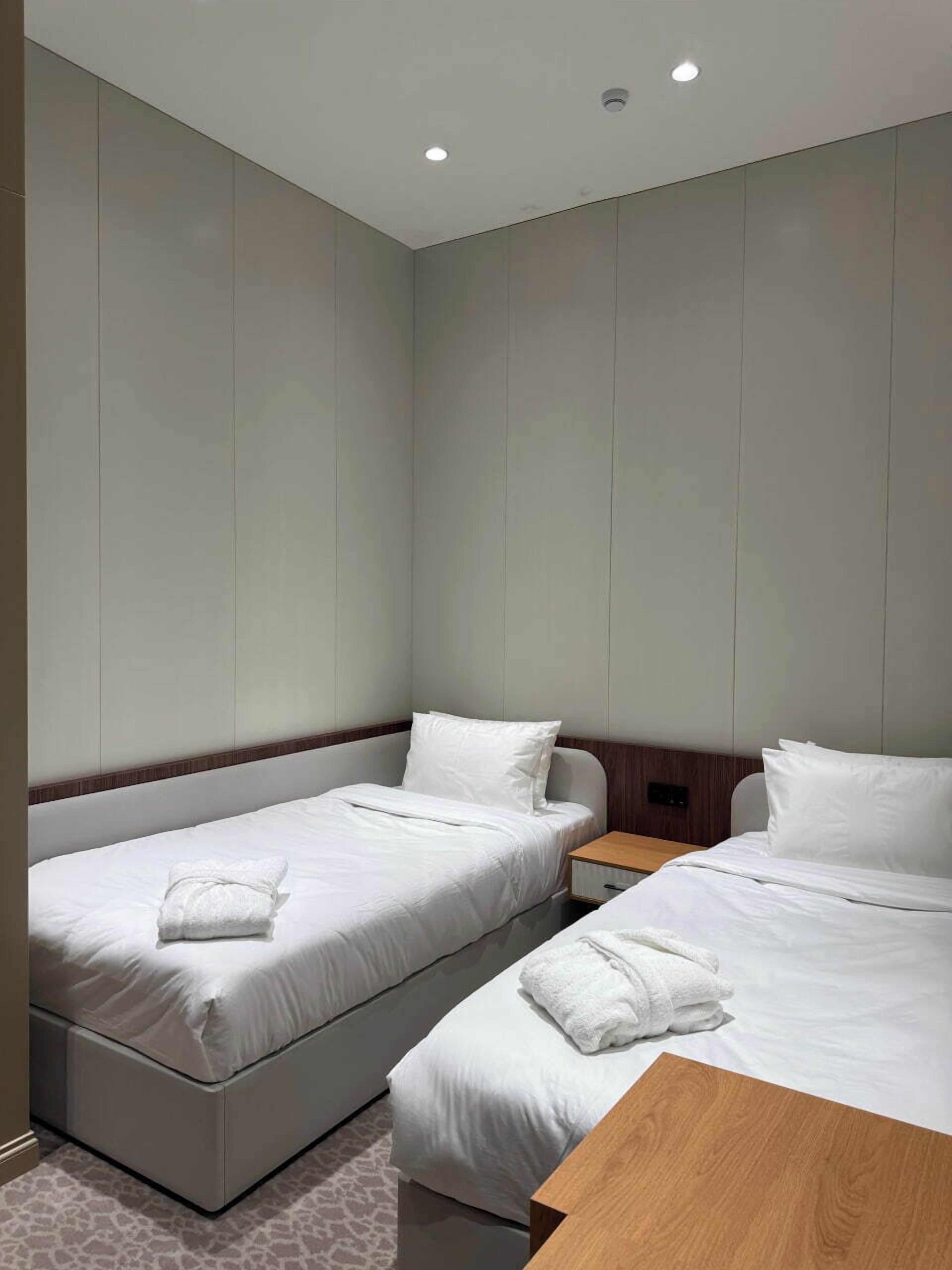 Ein Hotelzimmer mit zwei Einzelbetten, einem Holfnachtkästchen und einem kleinen Tisch.