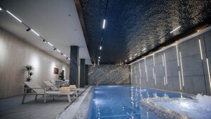 An indoor swimming pool with a tiled floor, lounge chairs, and a ceiling with a textured pattern. - AD Bellagio Hotel (Samarkand)