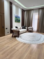 A modern living room with a beige sofa, two armchairs, a round rug, and a painting on the wall.