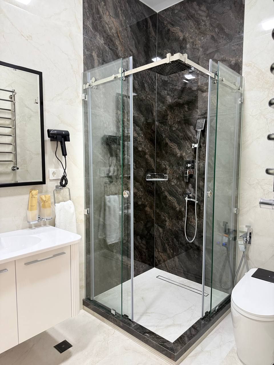 Une salle de bain moderne avec une douche en verre, un lavabo blanc et un sol carrelé en marbre.
