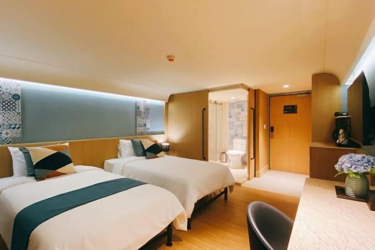 A hotel room with two beds, a desk, and a bathroom.