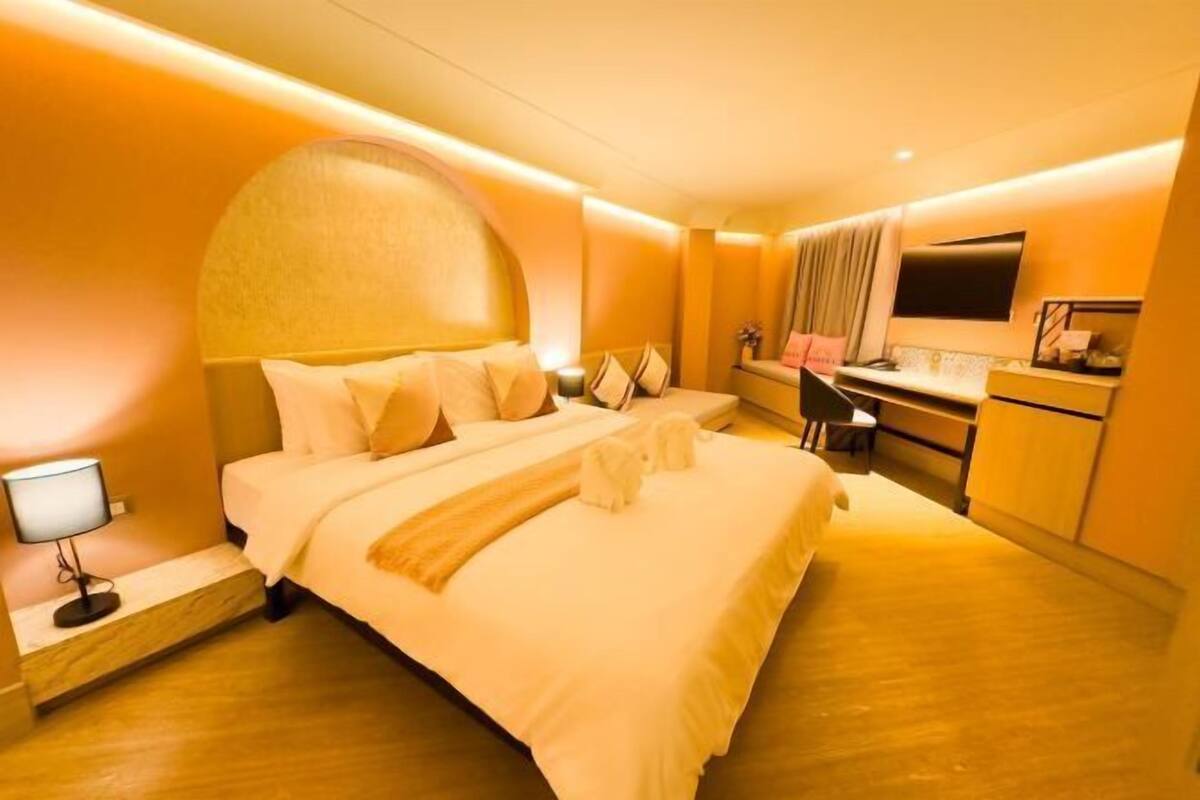 A hotel room with a large bed, a desk, a mirror, and a TV.