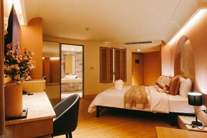 Habitació d'hotel amb llit, taula de nit, cadira i escriptori amb làmpada.