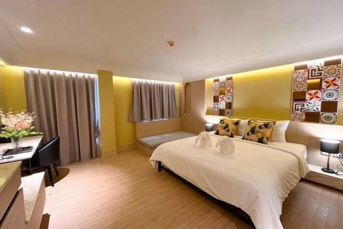 A hotel room with a bed, a desk, a chair, a window with curtains, and a wall with patterned decor.