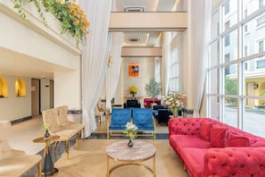 Un hall d’hôtel aménagé avec des espaces salon, un comptoir d’accueil et de grandes fenêtres.