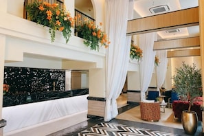 Un vestíbulo de hotel con una recepción, una escalera y un área de descanso con una planta.