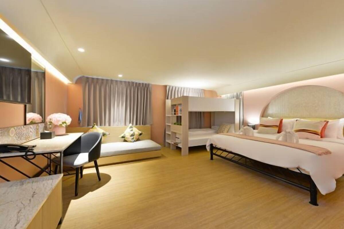 A modern hotel room with a bed, a desk, a chair, and a bookshelf.