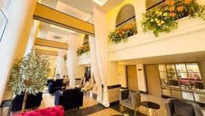 Een ruime lobby met een hoge plafond, modern meubilair en sierplanten.
