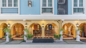 Een hotelentree met een overdekt terras, meerdere bogen en potplanten.