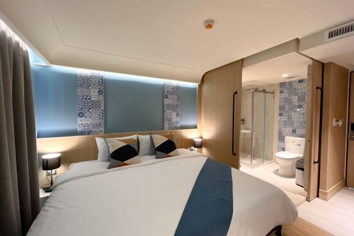 A hotel room with a bed, bedside table, lamp, and a bathroom with a toilet and shower.
