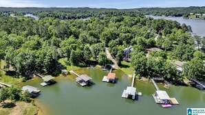 Vue aérienne d’une propriété au bord du lac, avec plusieurs bateaux amarrés, une jetée et une zone boisée en arrière-plan.