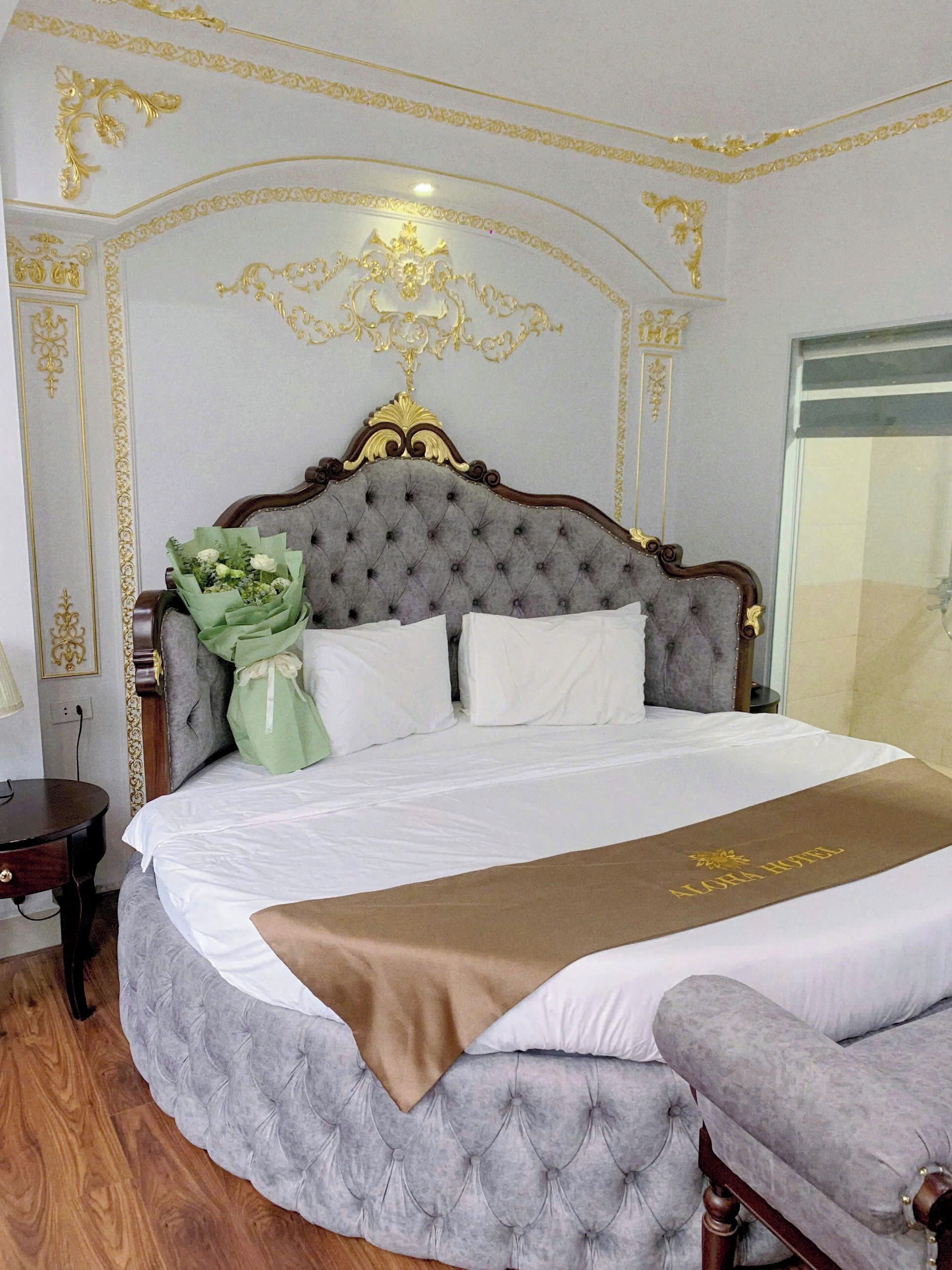A luxurious bedroom with a tufted headboard, a large bed with white linens, a brown throw blanket, and a green floral arrangement.