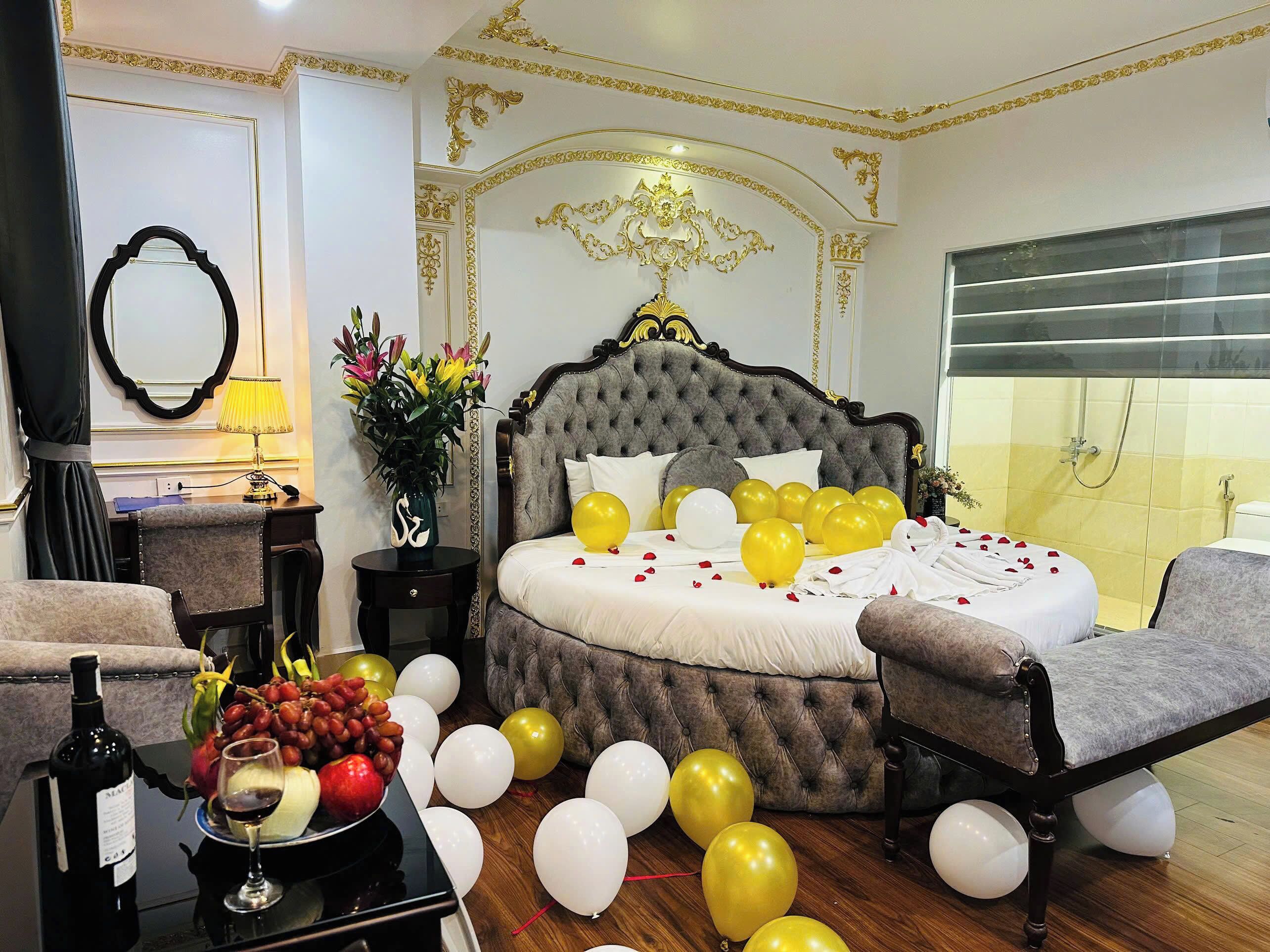 A luxurious bedroom with a tufted bed, a mirror, a desk with a lamp, and a vase with flowers.