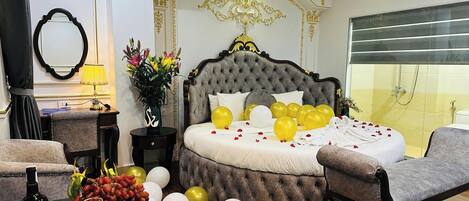 A luxurious bedroom with a tufted bed, a mirror, a desk with a lamp, and a vase with flowers.