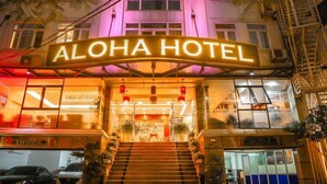 The exterior of Aloha Hotel with a prominent illuminated sign, a staircase leading to the entrance, and a visible parking area. - Aloha Hotel (Hanoi)