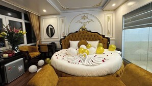 A luxurious bedroom with a large bed, a sitting area with a sofa and armchair, a desk, and a view of the city. - Aloha Hotel (Hanoi)