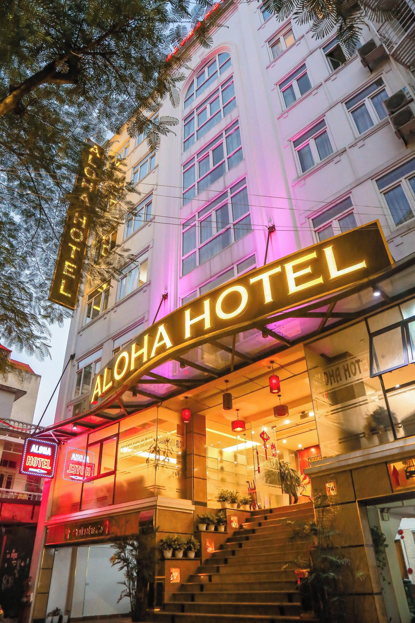 Un hotel con un llamativo letrero de neón, amplias ventanas y una escalera que conduce a la entrada.