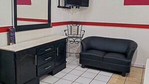 Une pièce avec un canapé noir, un téléviseur fixé au mur, un miroir et un meuble noir avec des tiroirs.