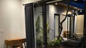 A modern hotel room with a large bed, a desk, a chair, and a sliding glass door leading to a balcony with a view of the outdoors. - Adyatma Ubud (Ubud)