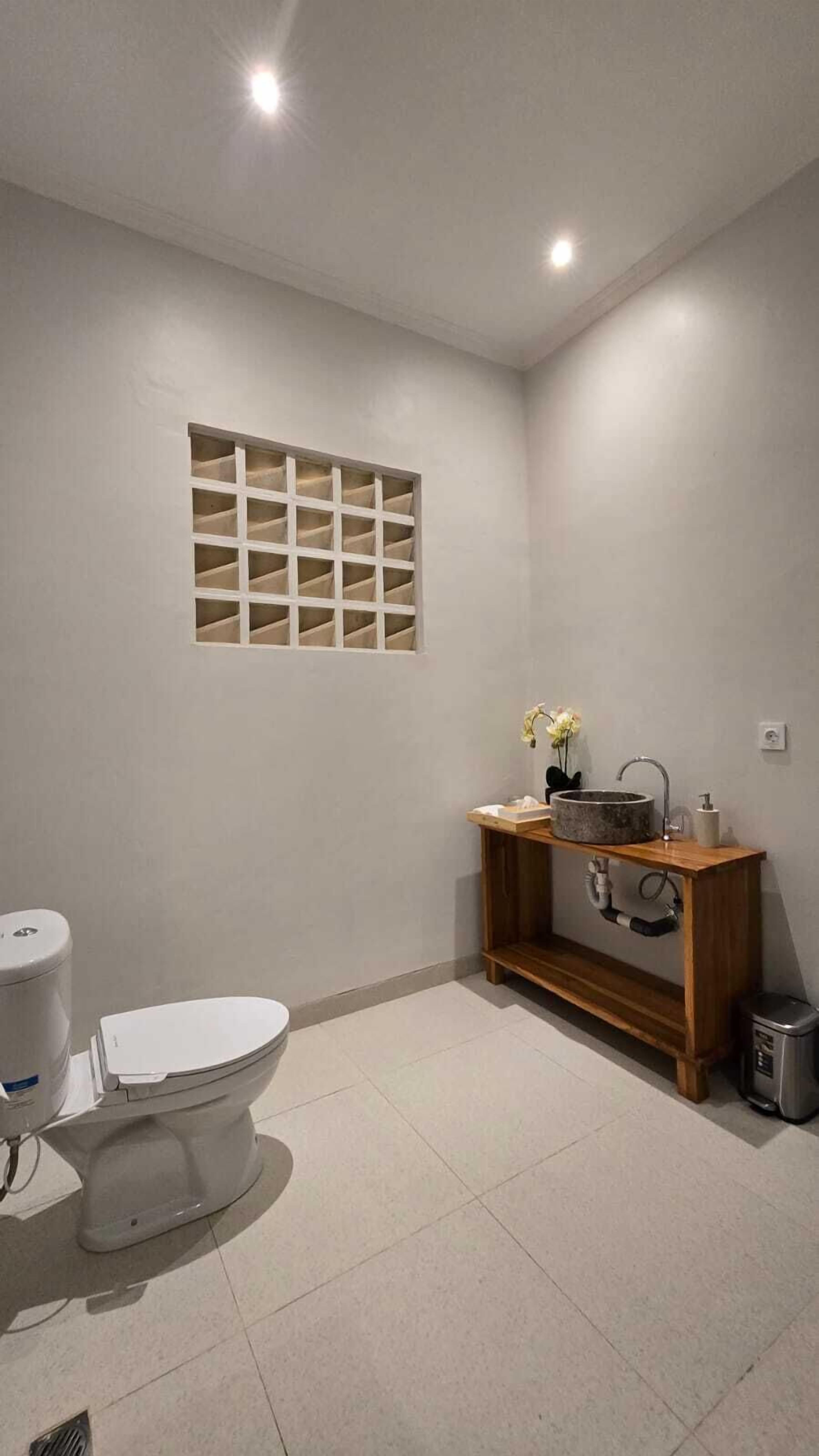 A bathroom with a toilet, a sink with a wooden vanity, and a window with a grid pattern.