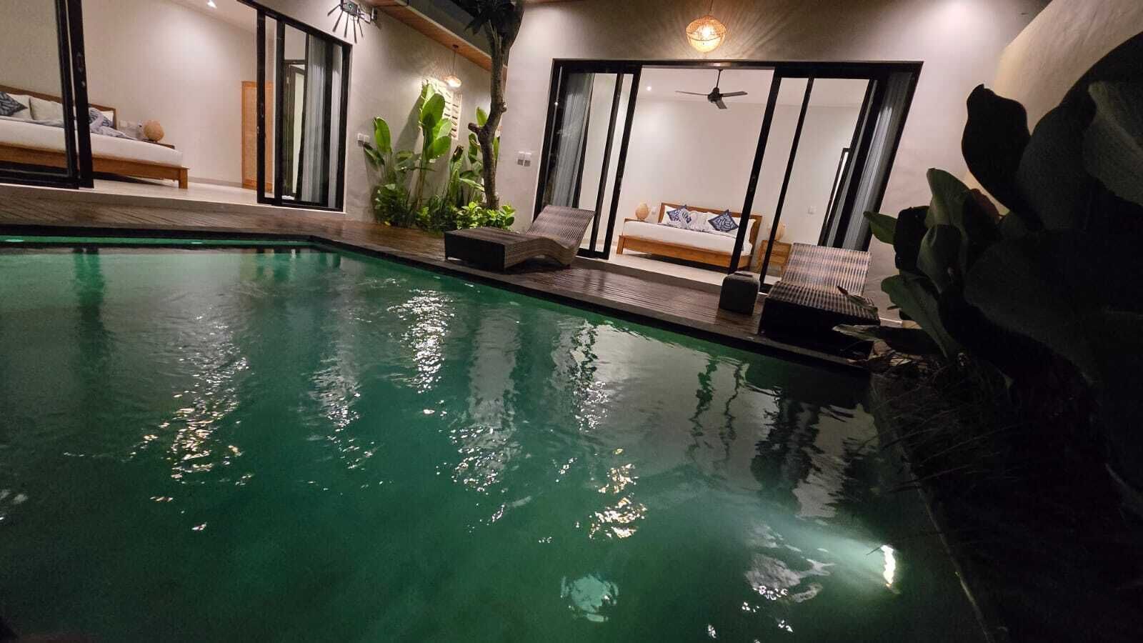 An indoor swimming pool with a lounge area, a bed, and a ceiling fan.