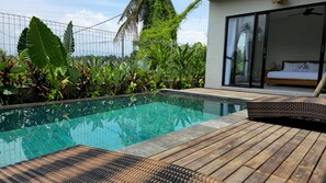 A swimming pool with a wooden deck, surrounded by lush tropical plants.