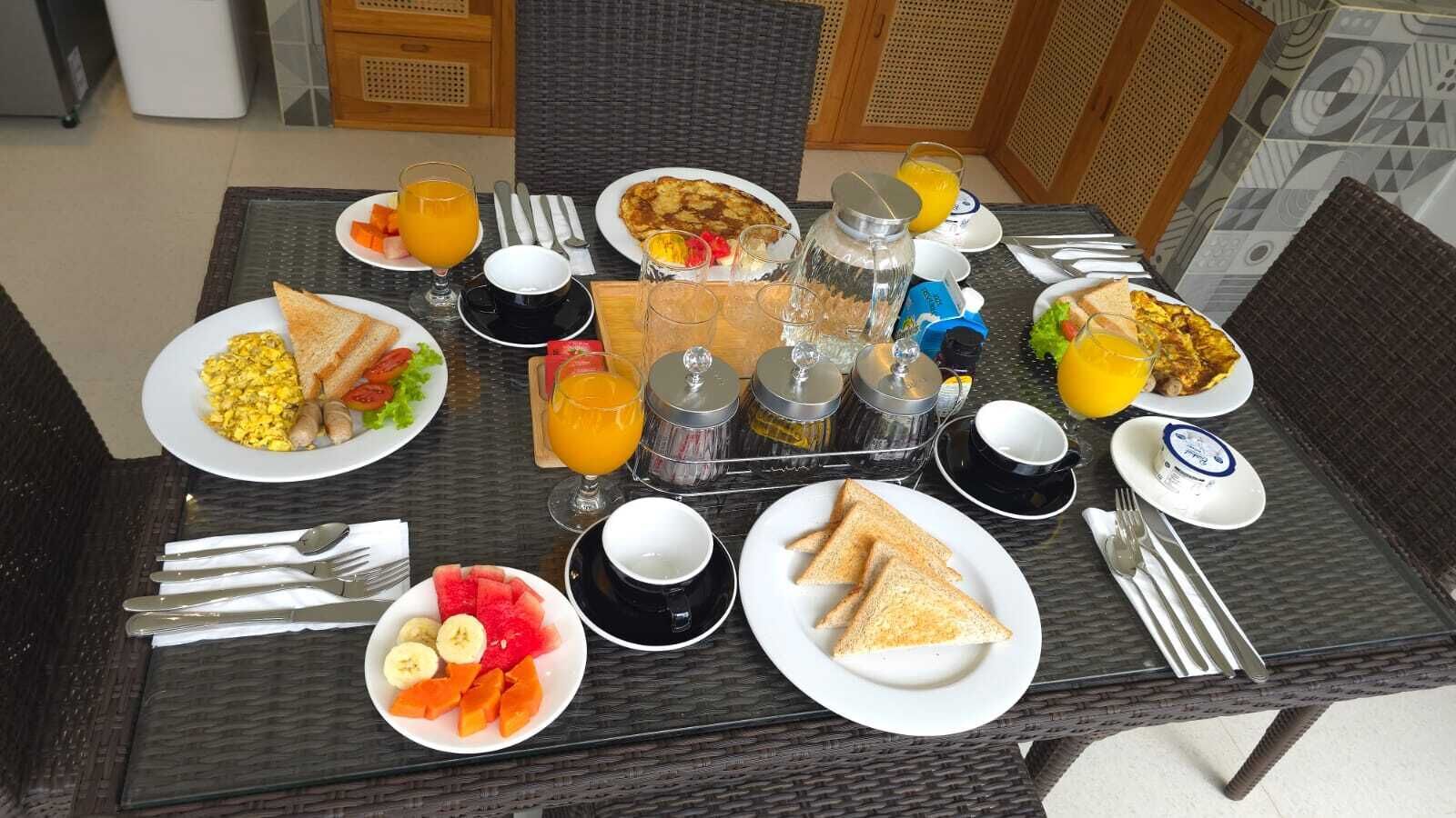 A breakfast table with plates of eggs, toast, fruit, and juice.