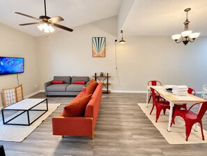A modern living room with a sofa, a dining table with chairs, a TV, and a ceiling fan. - Modern Top-Floor Loft w/ Pool, Balcony & Garden View! (Wilmington)
