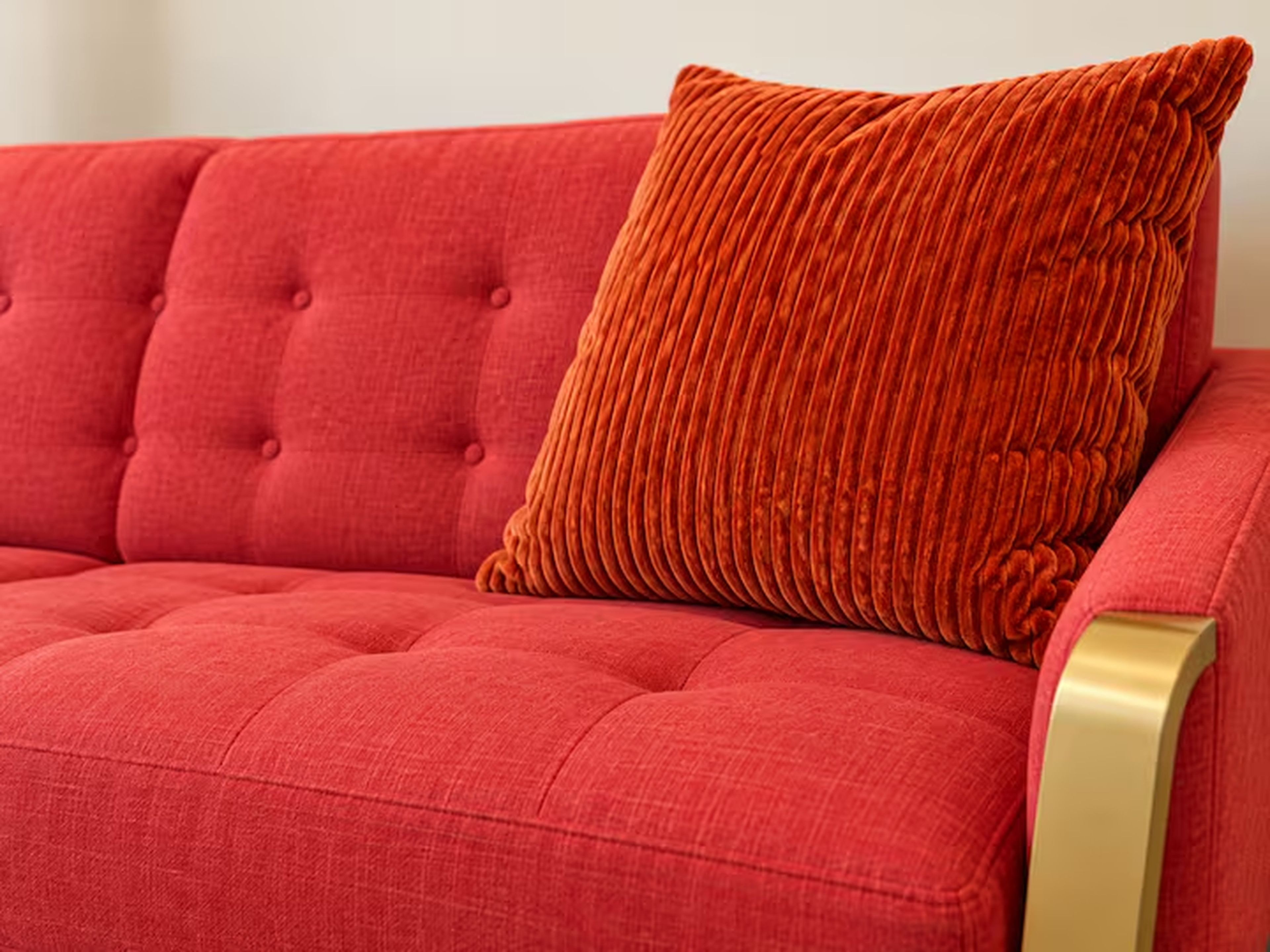 Ein rotes Sofa mit einer gepolsterten Rückenlehne und einem einzelnen orangefarbenen Kissen.