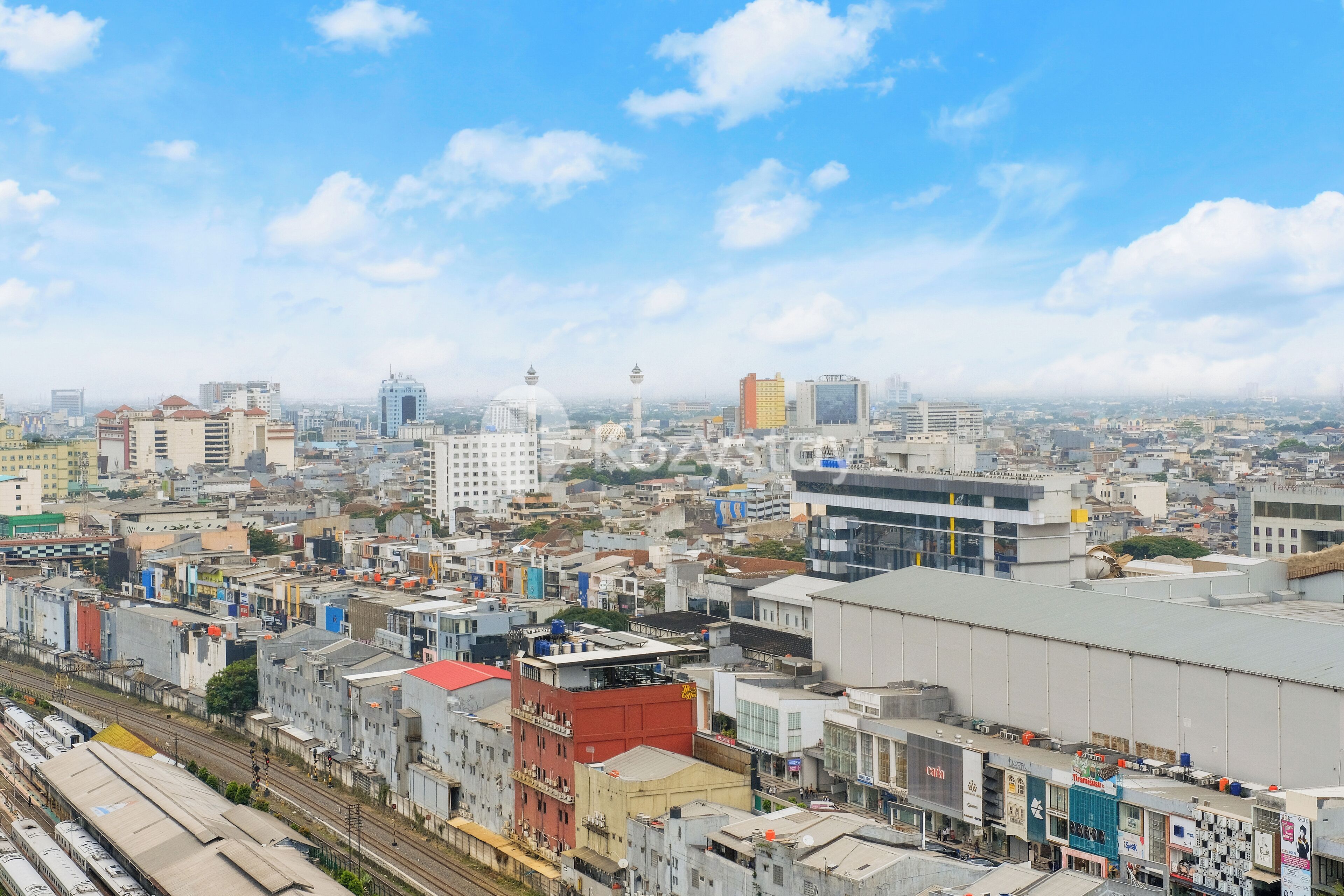 Un paisaje urbano con edificios residenciales y comerciales, una estación de tren destacada y un cielo despejado.
