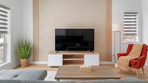 Una sala de estar moderna con una televisión de pantalla plana sobre un mueble de madera, un sillón rojo, un sofá gris y una mesa de centro de madera.